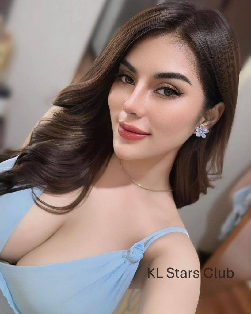 S-class Kuala Lumpur escort Victoria Qistina in a beige strapless dress, standing on a balcony with a city skyline at night.